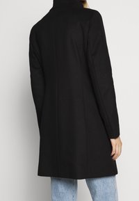 Black wool coat with a tailored shape, high collar, and clean lines. Smooth texture with a mid-length design and vented back detail.