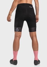 Schwarze Radshorts mit tailliertem Design, ausgestattet mit einem gepolsterten Sitz, strukturierten Seitenpanelen und einem reflektierenden Logo am Saum.