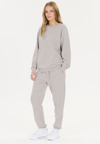 Grauer Sweatshirt und passende Jogginghose aus weichem Material. Das Outfit hat einen lockeren Schnitt, Bündchen und Seitentaschen, kombiniert mit weißen Sneakern.