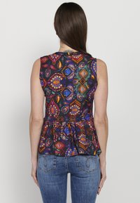 Színes peplum top, élénk virág- és geometriai mintával fekete háttéren, könnyű anyagból. Ujjatlan kivitel, ívelt alsó rész.
