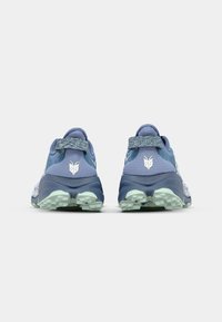 Baskets de sport bleues avec des tiges en maille texturée, un onglet au talon, un logo réfléchissant et un motif de semelle extérieure vert clair pour l'adhérence.