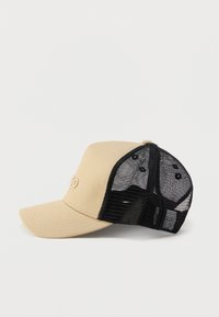 Μπεζ καπέλο μπέιζμπολ με μαλακό μπροστινό πάνελ και μαύρο πλέγμα πίσω, με οπές αερισμού και καμπυλωτό γείσο. Διακριτικό λογότυπο μπροστά.