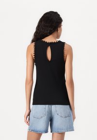 Svart ärmlös topp med ribbat mönster, scalloped halsringning och nyckelhålsdetalj bak. Kombination med ljusa denimshorts.