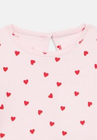 Ροζ κοντομάνικο τοπ με διασκορπισμένα κόκκινακαρδιές, με στρογγυλή λαιμόκοψη και άνοιγμα με κλειδί στην πλάτη.