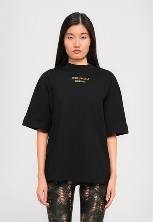 T-shirt noir oversize à manches courtes, avec une broderie dorée qui indique "JUST CAVALLI TRUE LOVER" sur la poitrine.