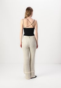 Svart spaghetti stropp bodysuit med en tettsittende silhuett, paret med beige teksturerte bukser med frynsete kanter og en avslappet passform.