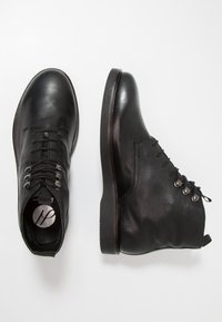 Černé kožené kotníkové boty s texturovaným svrškem, kulatou špičkou a šněrovacím uzávěrem. Obsahují stříbrné kroužky a plochou gumovou podrážku.