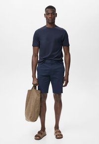 Marinblå kortärmad skjorta, marinblå shorts, bruna sandaler och en tan canvas tote-väska. Enkelt design med släta texturer och enhetlig färgschema.