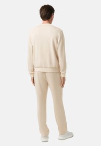 Helles beige Sweatshirt und passende Hose aus weichem Stoff, mit gerippten Bündchen und Gummizug, getragen mit weißen Turnschuhen.