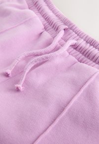 Pantalones deportivos de algodón rosa claro con tejido texturizado, que cuentan con una cintura elástica acanalada y cordones para ajustar.