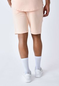 Pantaloni cargo pesca con una tasca laterale, caratterizzati da una texture liscia e un design a gamba dritta, abbinati a calze bianche a coste e sneakers.