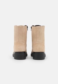 Botines de ante beige con suela de goma negra, que presentan un diseño elegante y cremalleras laterales para facilitar su uso.
