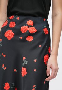 Melna auduma svārki ar dzīvīgu sarkanu rožu rakstu un zaļām lapām. Gluda tekstūra, pieguļošs dizains un vidēja garuma griezums.