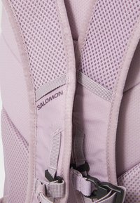 Les bretelles d'un sac à dos violet clair sont faites de mesh respirant et de tissu. Comprend des éléments réglables et une étiquette de logo. Texturé avec des détails de couture.