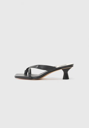 Sandale à talon en cuir noir avec un bout carré, dotée d'un design à lanières croisées et d'un talon cylindrique. Texture lisse avec un minimum de détails.