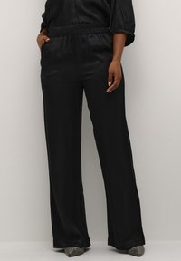 Pantalons larges noir en tissu lisse et texturé, dotés d'une taille élastique et de poches latérales. Accentués par des talons métalliques pointus.