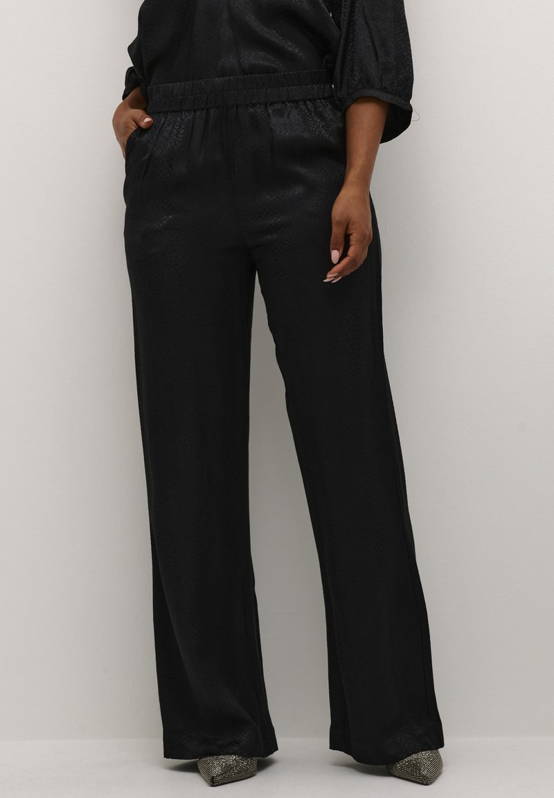 Pantalons larges noir en tissu lisse et texturé, dotés d'une taille élastique et de poches latérales. Accentués par des talons métalliques pointus.