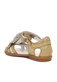 Goldene metallische Sandalen mit ausgeschnittenem Design, ausgestattet mit einem gepolsterten Riemen und einer strukturierten Oberfläche. Die braune Gummisohle sorgt für Stabilität.