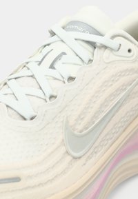 Ανοιχτό γκρίζο και λευκό Nike Vomero παπούτσι τρεξίματος με υφασμάτινη επιφάνεια, κλείσιμο με κορδόνια και χοντρή σόλα με ροζ λεπτομέρειες. Περιλαμβάνει το χαρακτηριστικό swoosh.