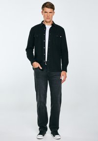 Camicia in denim nero con frontale a bottoni, abbinata a jeans scuri e sneaker nere. La camicia presenta due tasche sul petto e una vestibilità classica.
