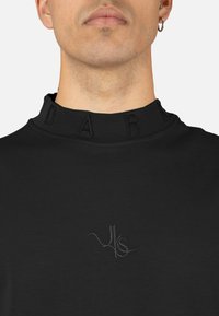 Sudadera negra con un cuello alto texturizado con letras en relieve "D A R" y un logo sutil bordado en el pecho.