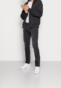 Svart bomberjacka med ribbade muddar, vit t-shirt, mörka jeans och vita sneakers. Outfitten har en avslappnad och åtsittande design.
