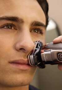 Philips elektrisch scheerapparaat met een zwart en zilver lichaam, ergonomische grip en een slank, gebogen ontwerp, gepositioneerd nabij het gezicht van de gebruiker.