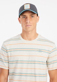 Men's short-sleeve shirt, light beige with horizontal teal and orange stripes, round neckline. Black cap with a patch logo and light blue accents.