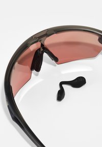 Sonnenbrille mit einem gebogenen dunkelgrauen Rahmen und rot getönten Gläsern; umfasst schwarze Gummigriffe an den Bügeln und verstellbare Nasenpads.