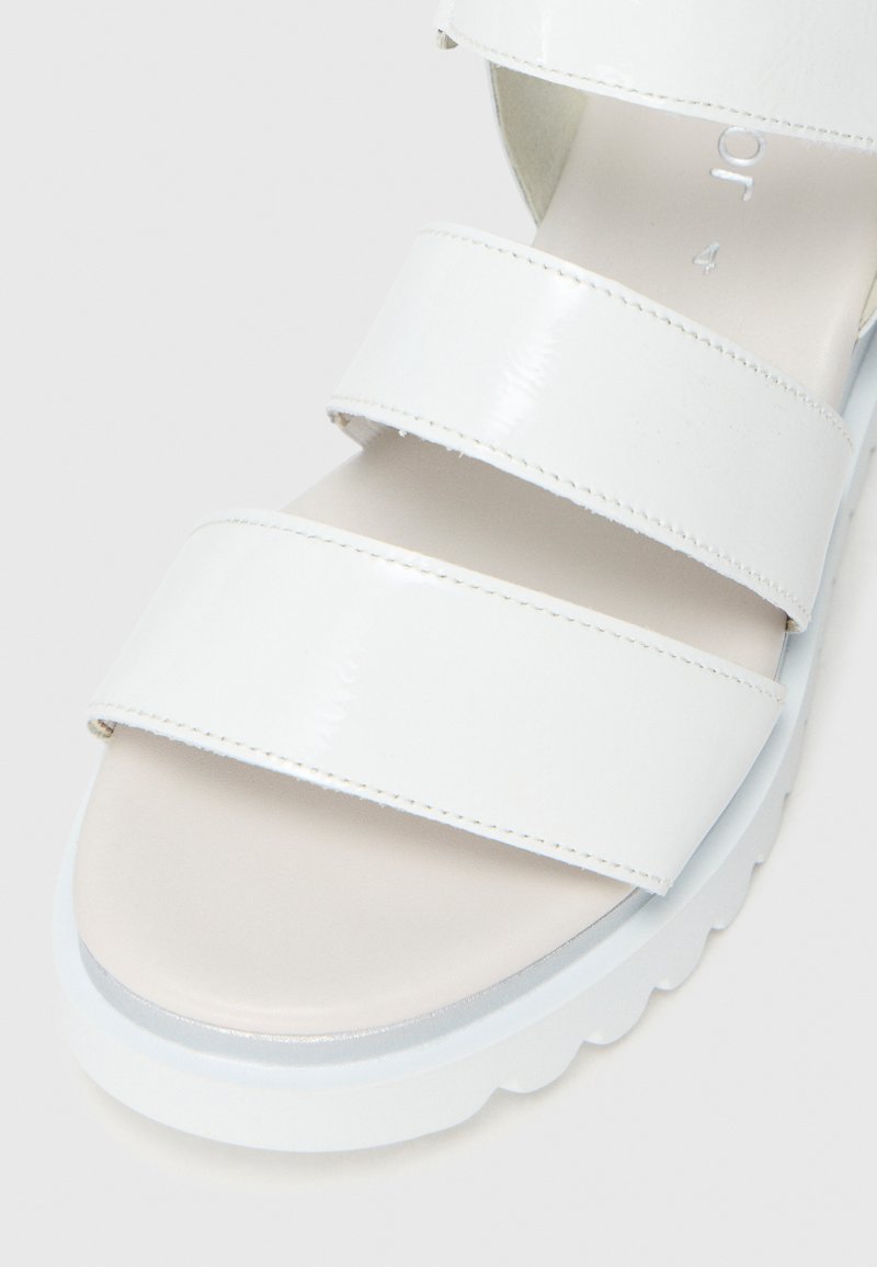 Sandalia de charol blanca con tres correas horizontales, plantilla acolchada de color beige claro y suela texturizada de color azul claro.
