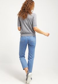 Grå kortärmad tröja med vit kant, tillsammans med medelblå raka jeans. Sneakers är gråa med en vit sula; texturerat hår.