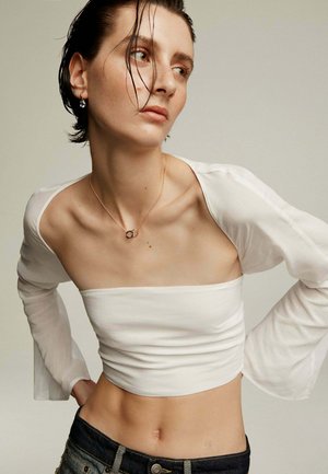 Top blanco corto de manga larga con textura fruncida, combinado con jeans de mezclilla oscuros. Diseño minimalista con escote cuadrado y un brillo sutil.