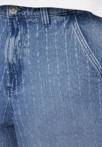 Jean en denim bleu clair avec des rayures verticales décolorées, présentant une taille standard et un design de poches, ainsi qu'une finition en tissu texturé.