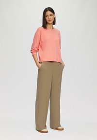 Lichtroze sweatshirt met verlaagde schouders, gecombineerd met beige wijde broek. Schoenen hebben een crèmekleurige accenten op de neus.