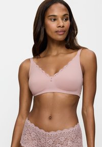 Reggiseno wireless rosa chiaro con bordo in pizzo lungo il scollo e un bottone decorativo al centro. Tessuto liscio con un design senza cuciture.