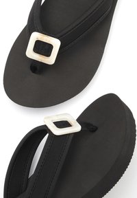 Black flip-flops featuring a soft, textured sole and black fabric straps. A square, cream-colored accent decorates the strap's intersection.
