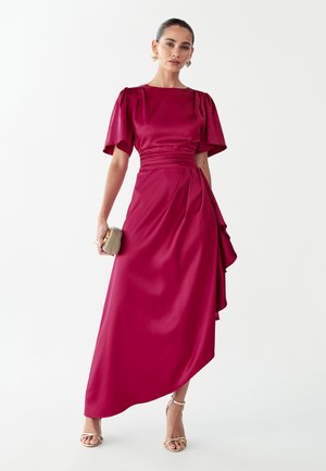 Fuksia satiinist kleit lühikeste paftvarrukatega, keha järgiva ülakeha ja külje drapeeringuga, millele lisandub kuldne käekott ja rihmikad sandaalid.