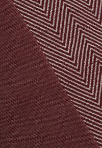 Burgundy fabric split diagonally; the left side has a smooth texture, while the right features a white zigzag pattern against the base.