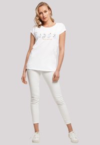 White cotton t-shirt with short sleeves, front graphic featuring cartoon characters, paired with white slim-fit pants and white sneakers.