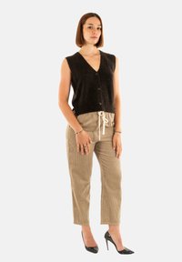 Gilet senza maniche nero in maglia con scollo a V e bottoni, abbinato a pantaloni in corduroy color cammello e tacchi alti neri. Design semplice e aderente.