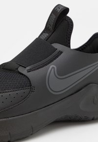 Schwarzer Sportschuh mit einem Obermaterial aus Mesh, elastischem Riemen und strukturiertem Gummisohle. Auffälliges graues Nike-Logo und glatte synthetische Akzente.