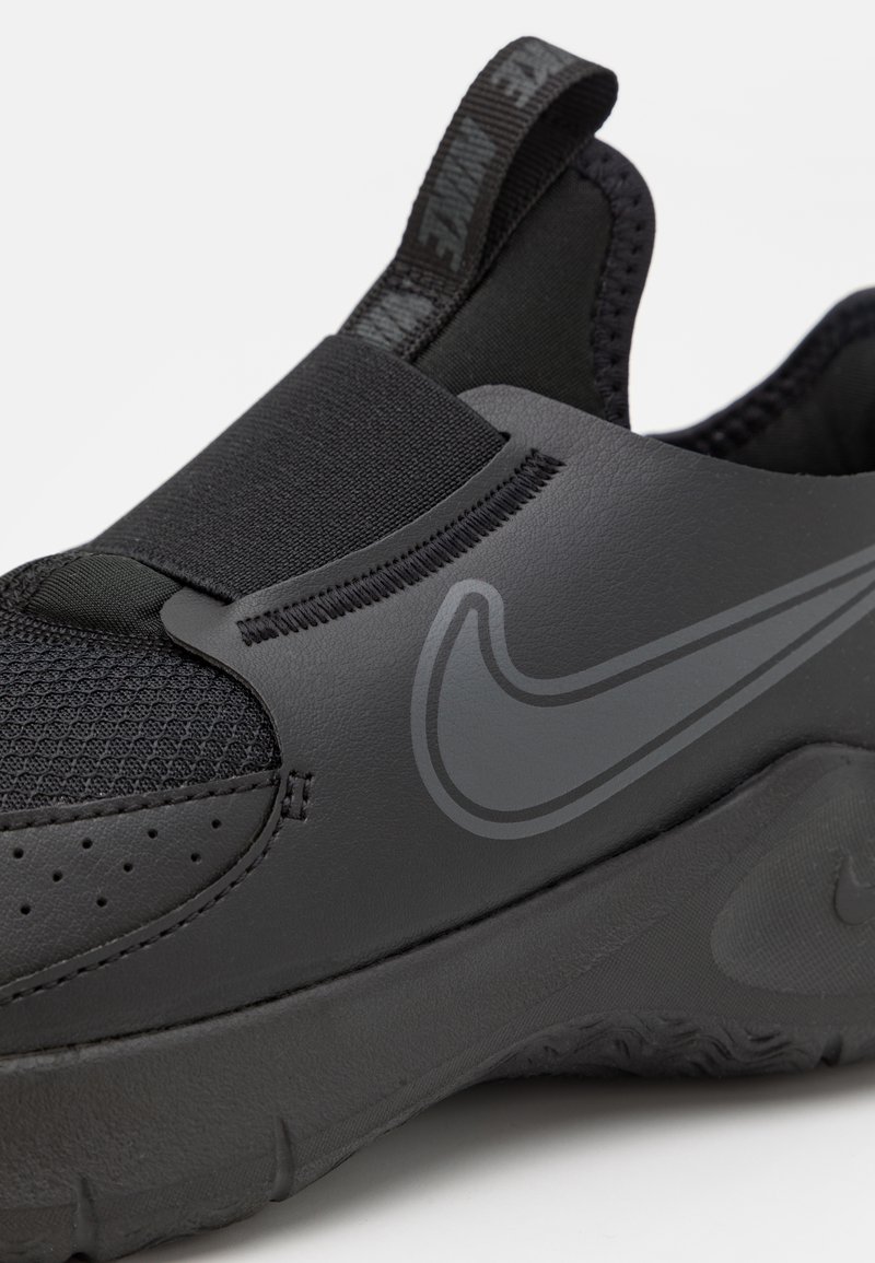 Chaussure de sport noire avec une tige en mesh, une bande élastique et une semelle en caoutchouc texturée. Logo Nike gris notoire et accents en synthétique lisse.