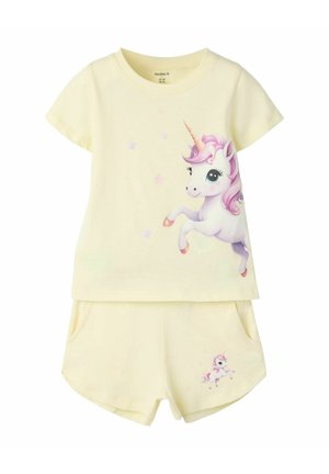 Krémová detská sada trička a šortiek so zobrazením jednorožca s ružovou hrivou a hviezdičkami na tričku a menším jednorožcom na šortkách.
