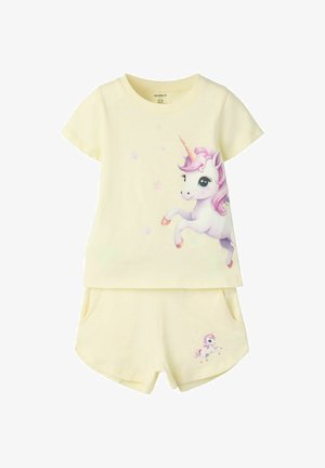 Børnesæt med cremefarvet t-shirt og shorts med en grafik af en enhjørning med lyserød manke og stjerner på t-shirten og en mindre enhjørning på shortsene.