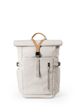 Light beige roll-top backpack with front zipper pocket, tan leather handle and strap, side pockets, and black buckle closure.