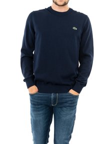 Suéter de cuello redondo azul marino hecho de algodón, con un logo verde de Lacoste. Puños y dobladillo acanalados, combinado con jeans de color azul claro.