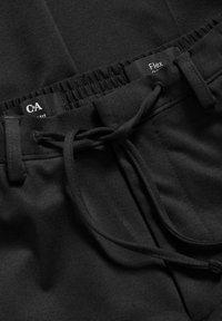 Svarta joggingbyxor med elastiskt midjeband, justerbar dragsko och subtil textur. Etiketterna visar varumärke och passformsdetaljer.