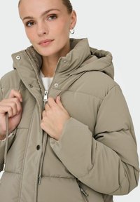 Beige dunjakke med hætte, der har lynlås- og trykknaplukninger, justerbare snore og sidelommer. Glat, quiltet tekstur.