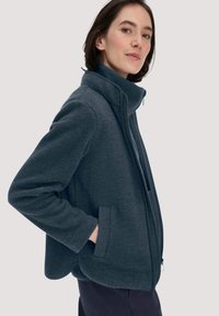 Donkerblauwe fleecejack met een hoge kraag, ritssluiting aan de voorkant en zijzakken. Zachte textuur en gestructureerd ontwerp met een ontspannen pasvorm.