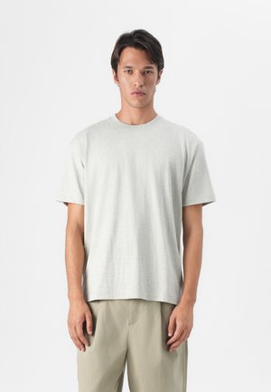 T-shirt en coton gris clair avec un col ras du cou et des manches courtes, affichant une coupe décontractée et une texture lisse, porté avec un pantalon beige.